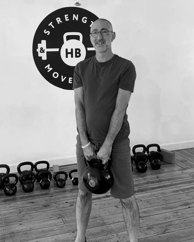 Martin standing in the studio holding a kettlebell, the Strength & Movement logo on the wall behind
