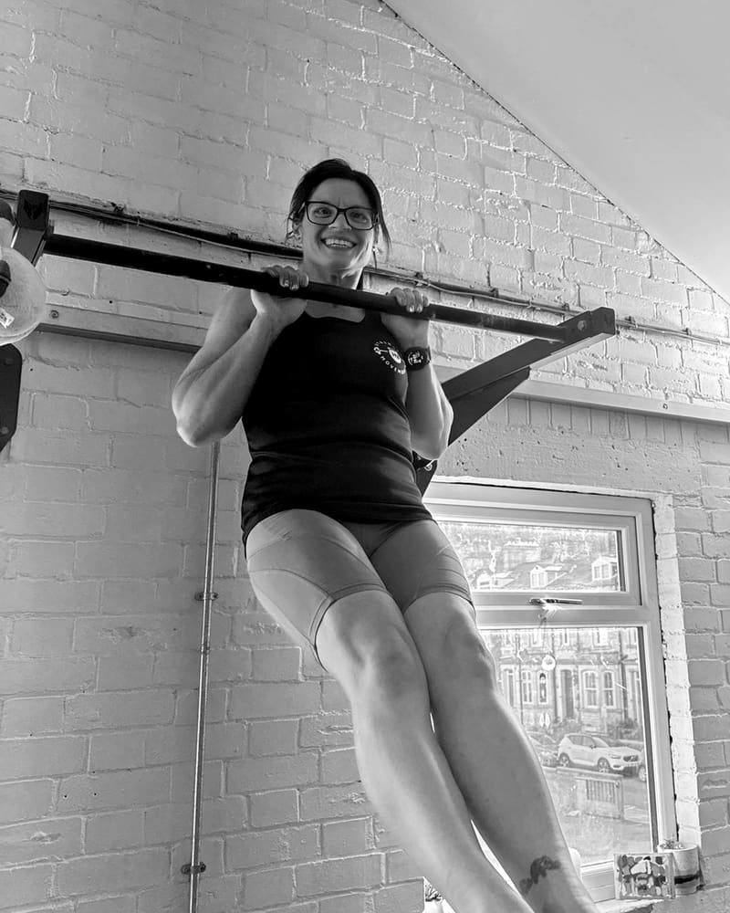 Mary smiling while hanging from a pull-up bar in the studio, legs raised