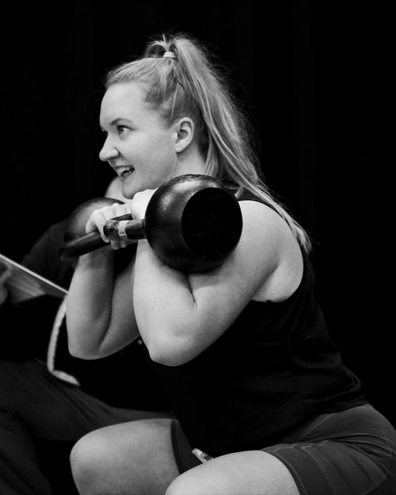 Nele smiling mid-squat, holding a kettlebell in the rack position