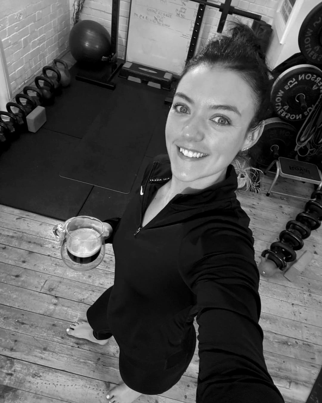 Megan Kelly smiling in the studio with a coffee, kettlebells and plates behind her