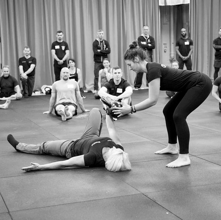 Megan coaching a client through a kettlebell get-up in front of a group